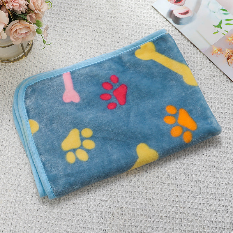 Blue pet blanket with colorful paw and bone patterns on a textured surface.