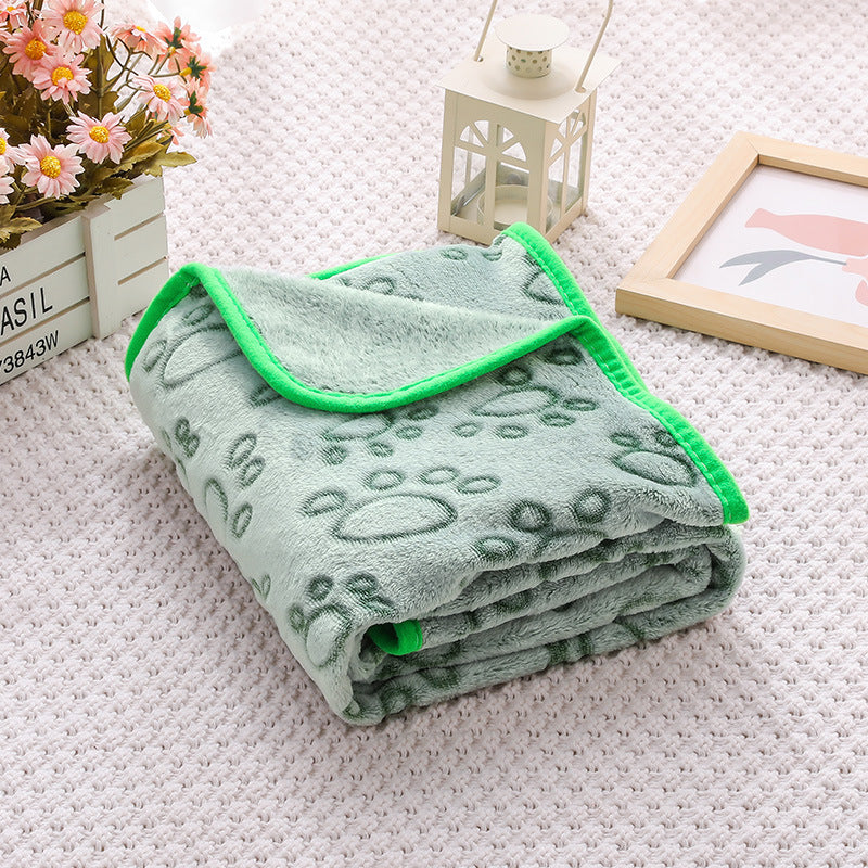 Folded green blanket with floral patterns on a textured surface with decorative items.